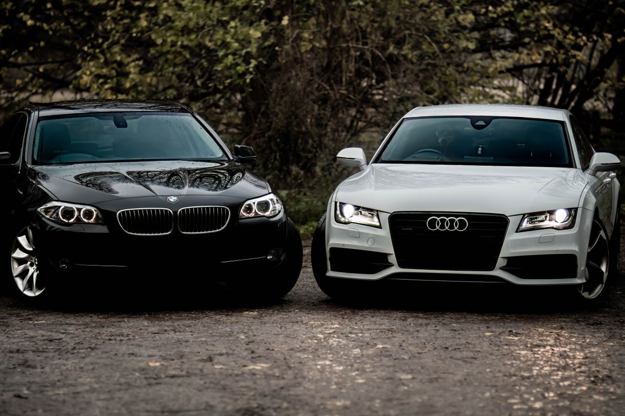 services-05 Black BMW and white Audi luxury sedans parked outdoors on a gravel path.
